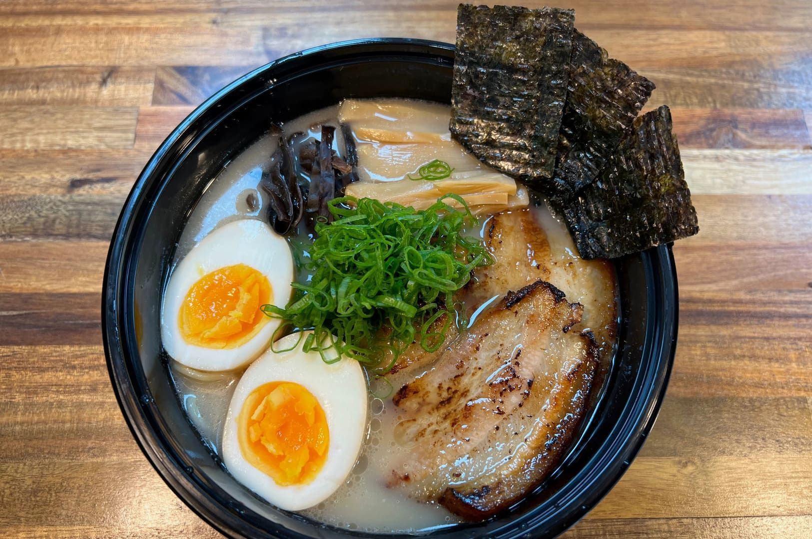 Tonkotsu Black Ramen served in a bowl, featuring eggs, meat slices, and assorted vegetables.