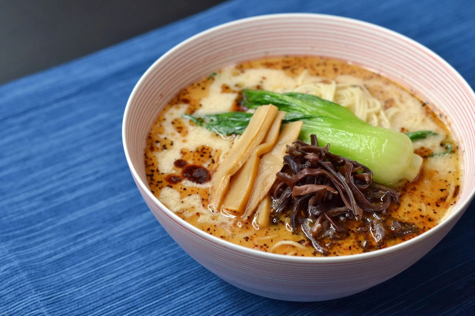 A bowl of Tonkotsu Black Ramen featuring rich noodles topped with fresh vegetables.