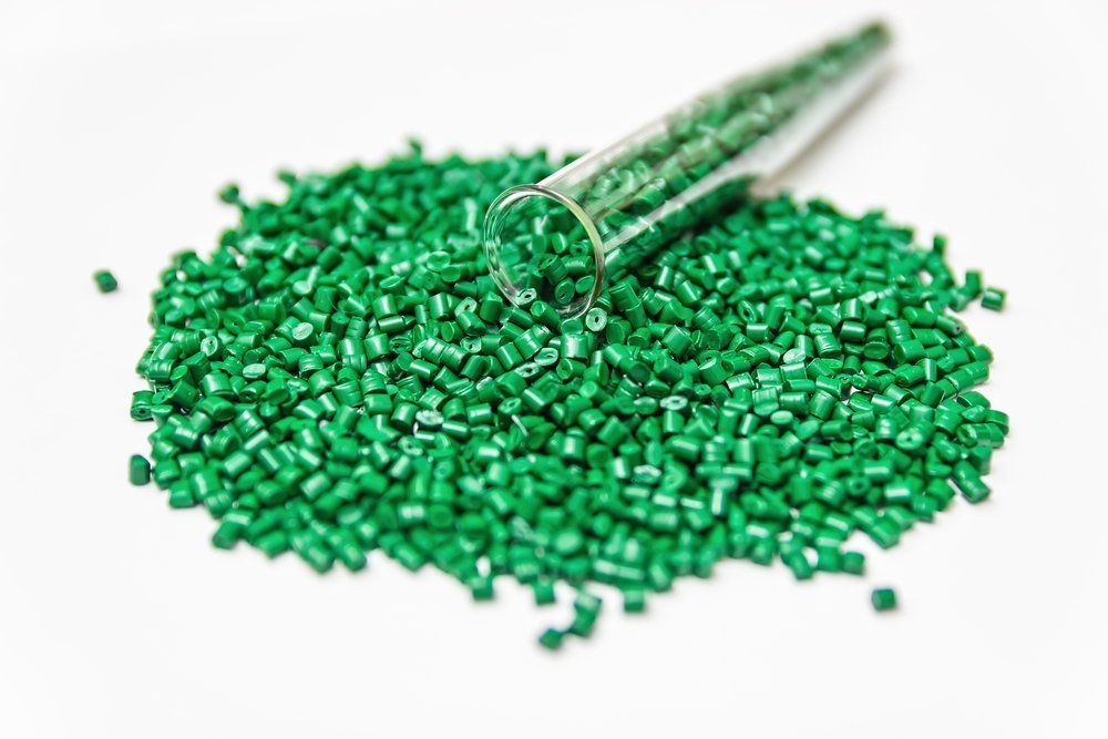 A glass tube is pouring green plastic granules into a pile.