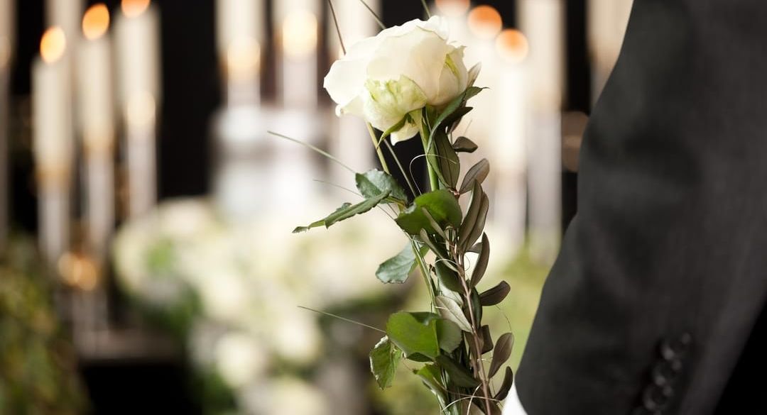 A man in a suit is holding a white rose at a funeral.