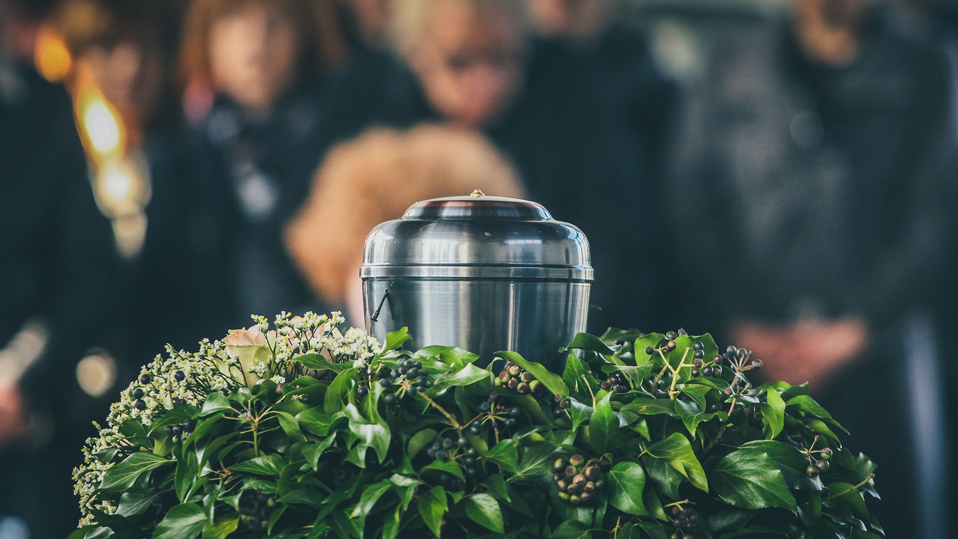 A urn is sitting on top of a wreath of leaves at a funeral.