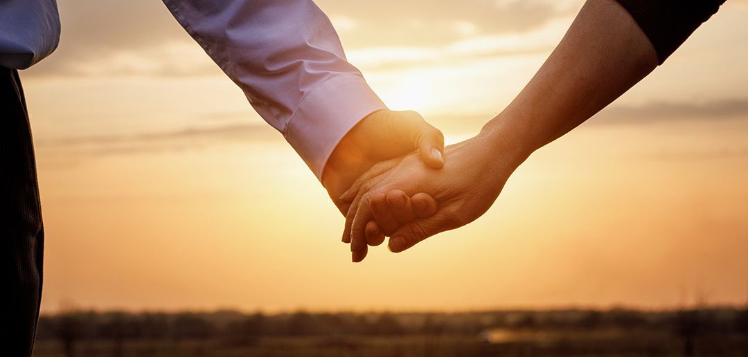 A man and a woman are holding hands at sunset.