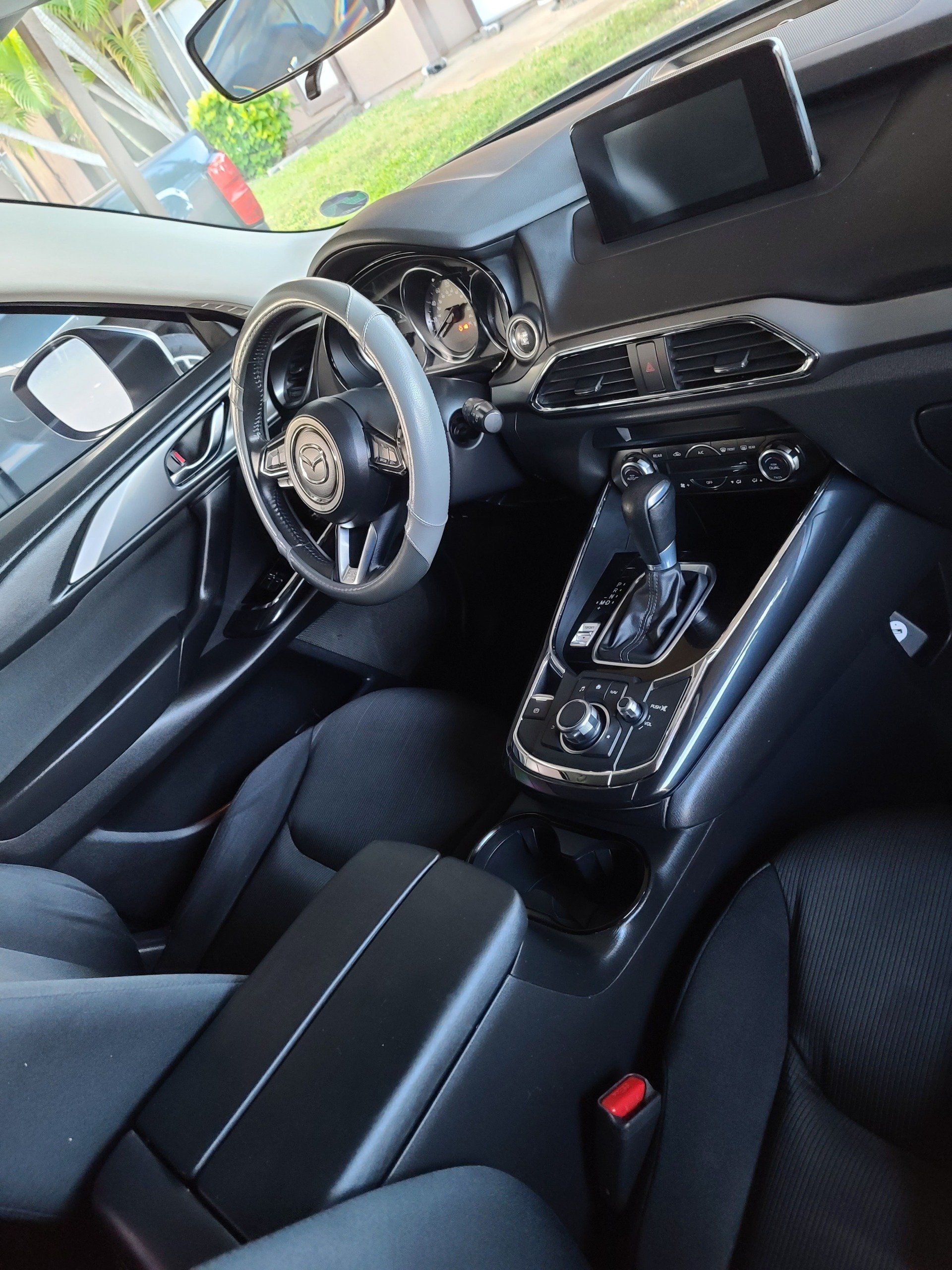 Interior view of a black car with a steering wheel cover, dashboard, console, and seats.