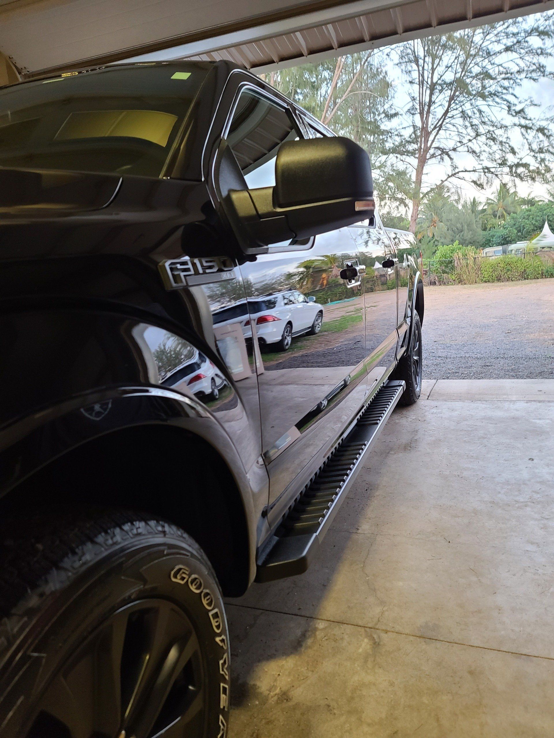 Black Ford F-150 truck parked in a garage. Side view showing the tire, running board, and mirror.