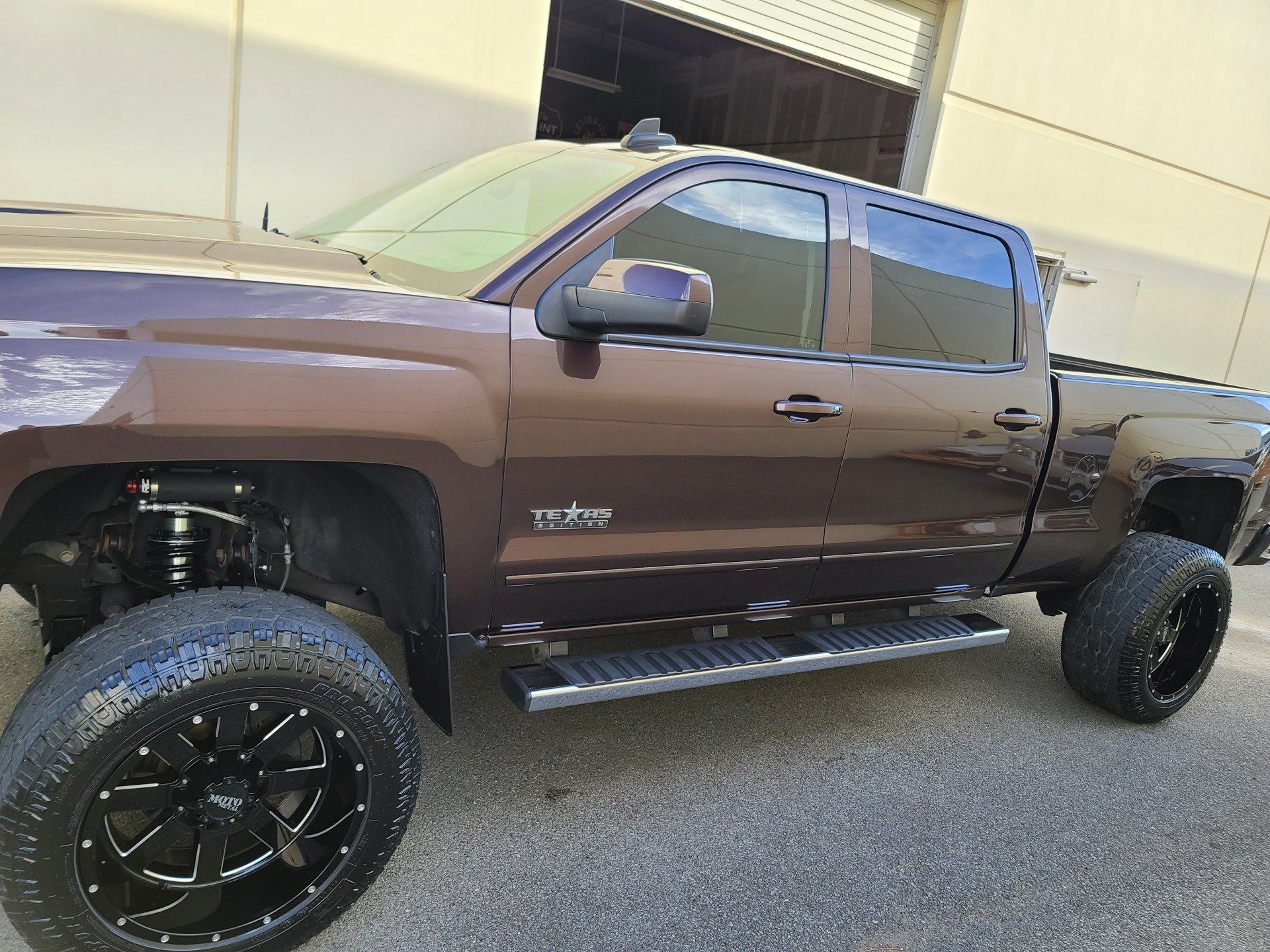 Brown lifted pickup truck with black wheels and running boards.
