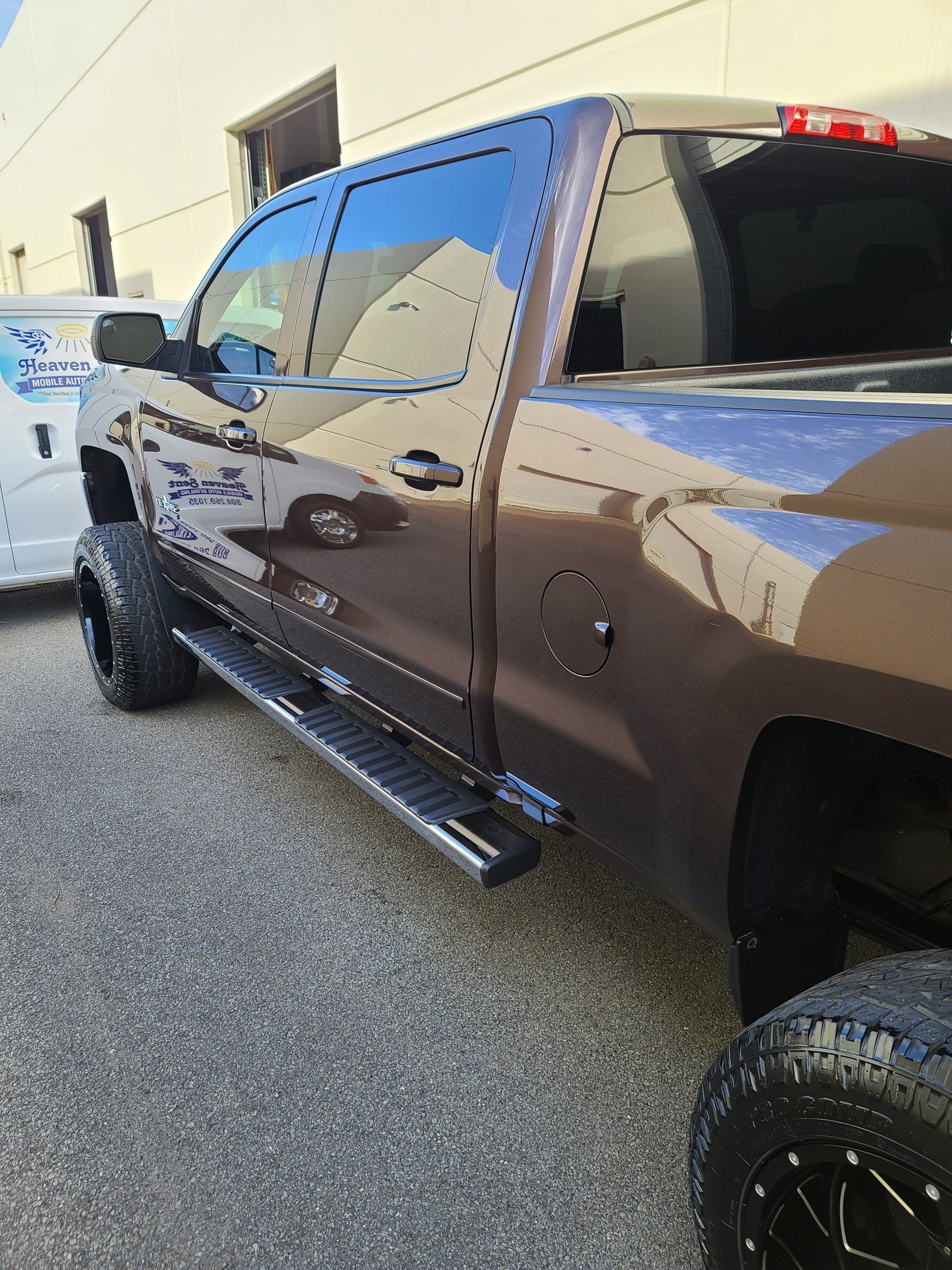 Brown pickup truck with large black tires, side steps, parked on pavement.