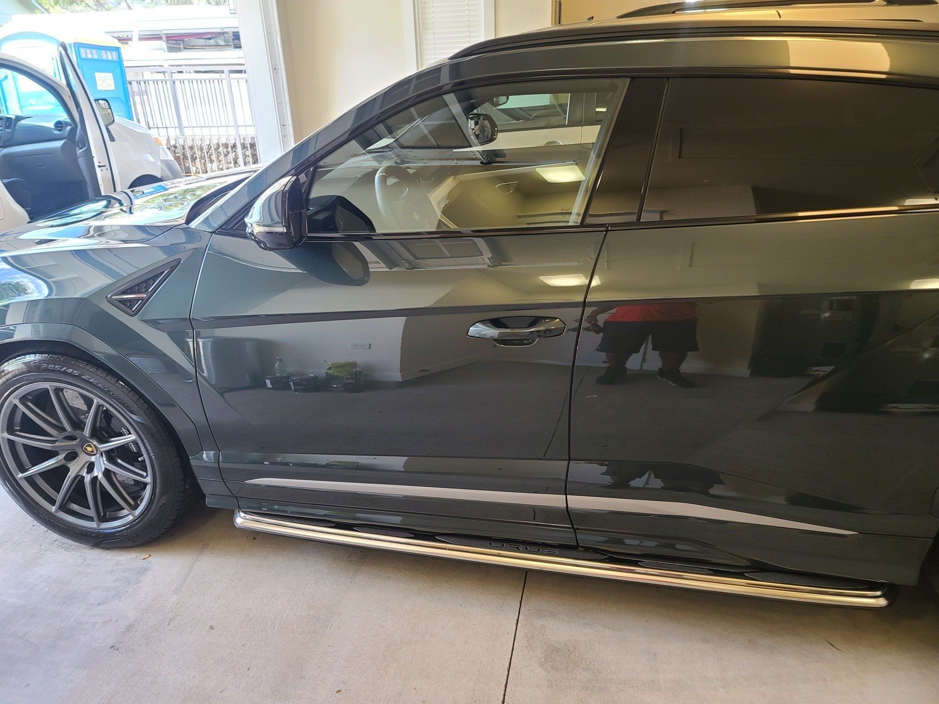 Dark green SUV with chrome running boards parked in a garage; tinted windows, part of a vehicle in the left background.