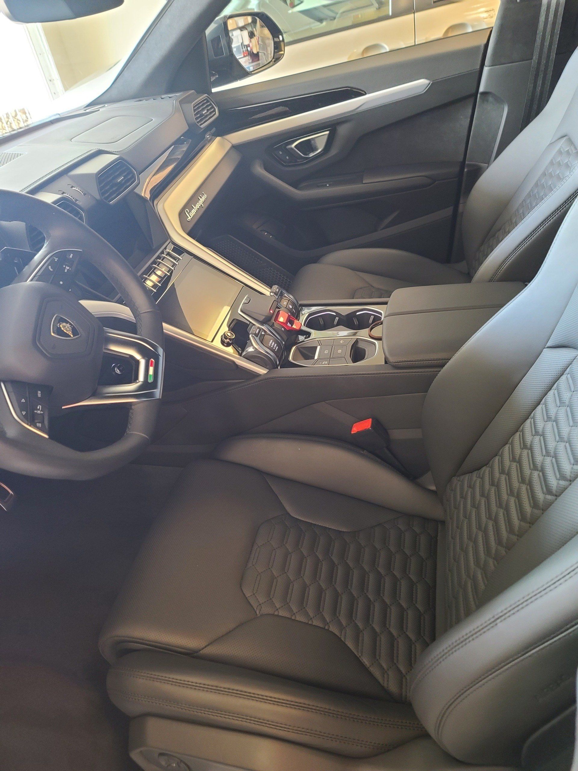 Interior of a black Lamborghini Urus SUV; black leather seats, dashboard, steering wheel, and console.