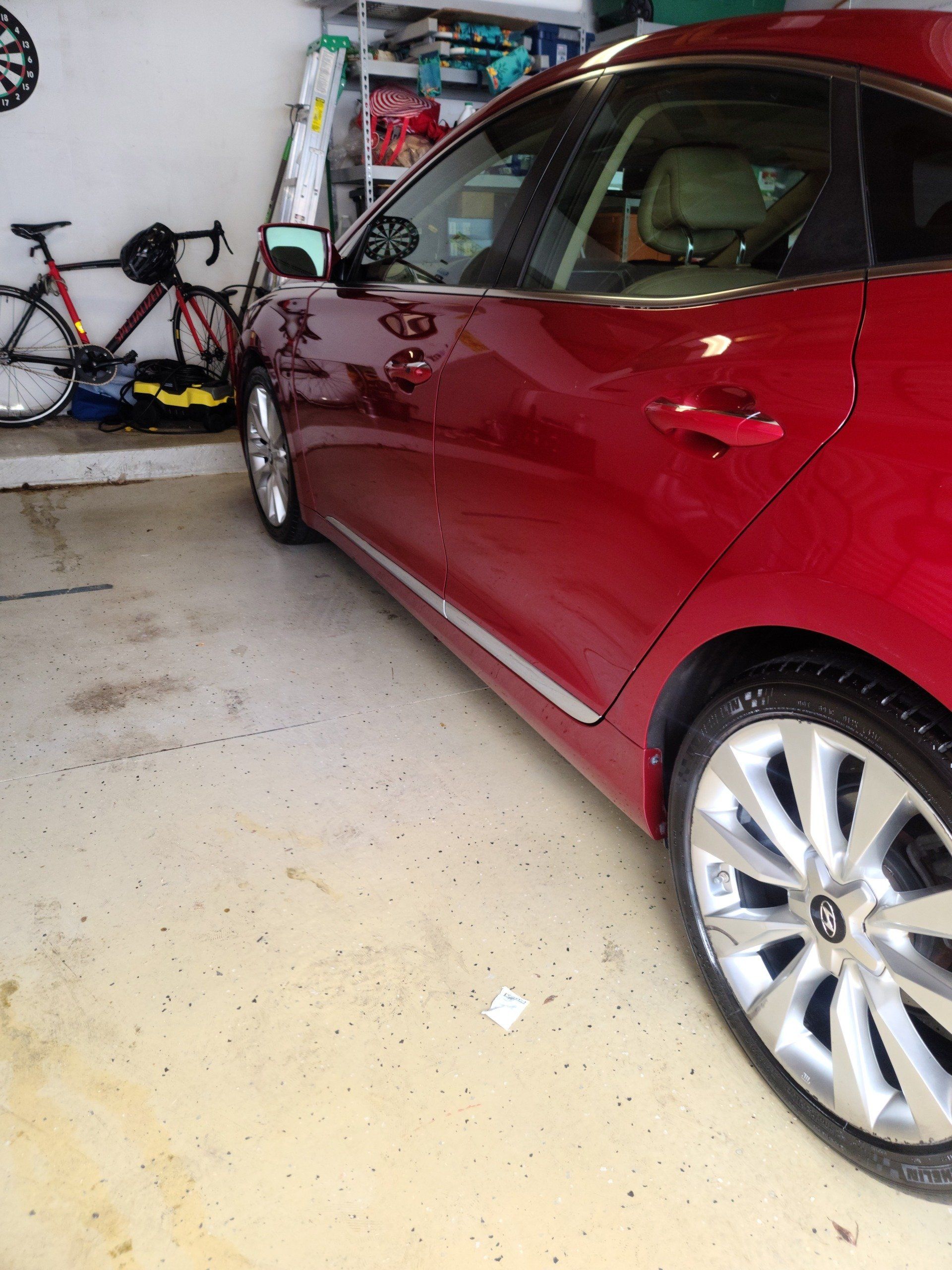 Red car parked in a garage with a bicycle in the background.