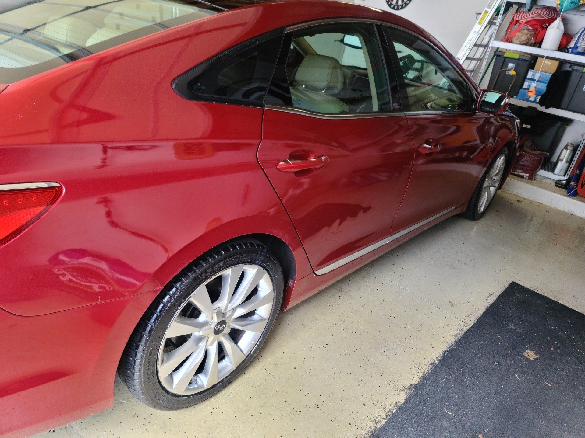 Red car parked in a garage with a black mat. Shiny, silver wheels.