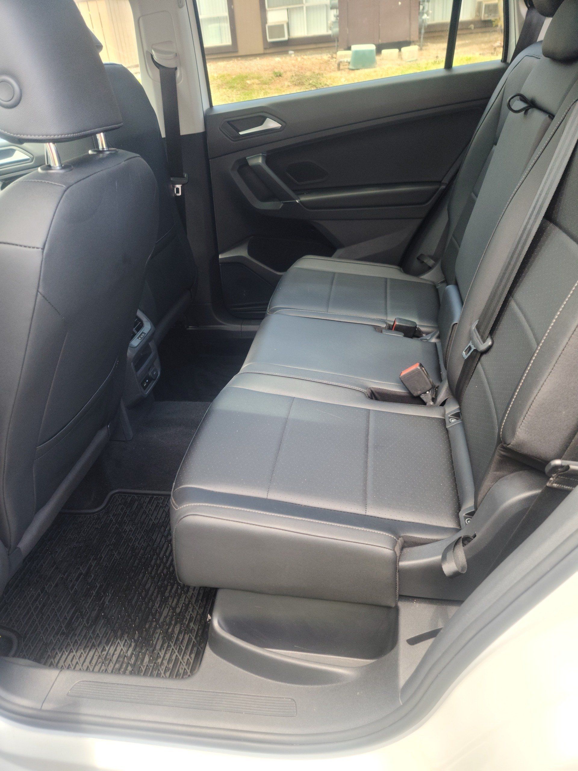 Interior view of a car's back seat. Black leather seats with seatbelts, a black floor mat, and a window visible.