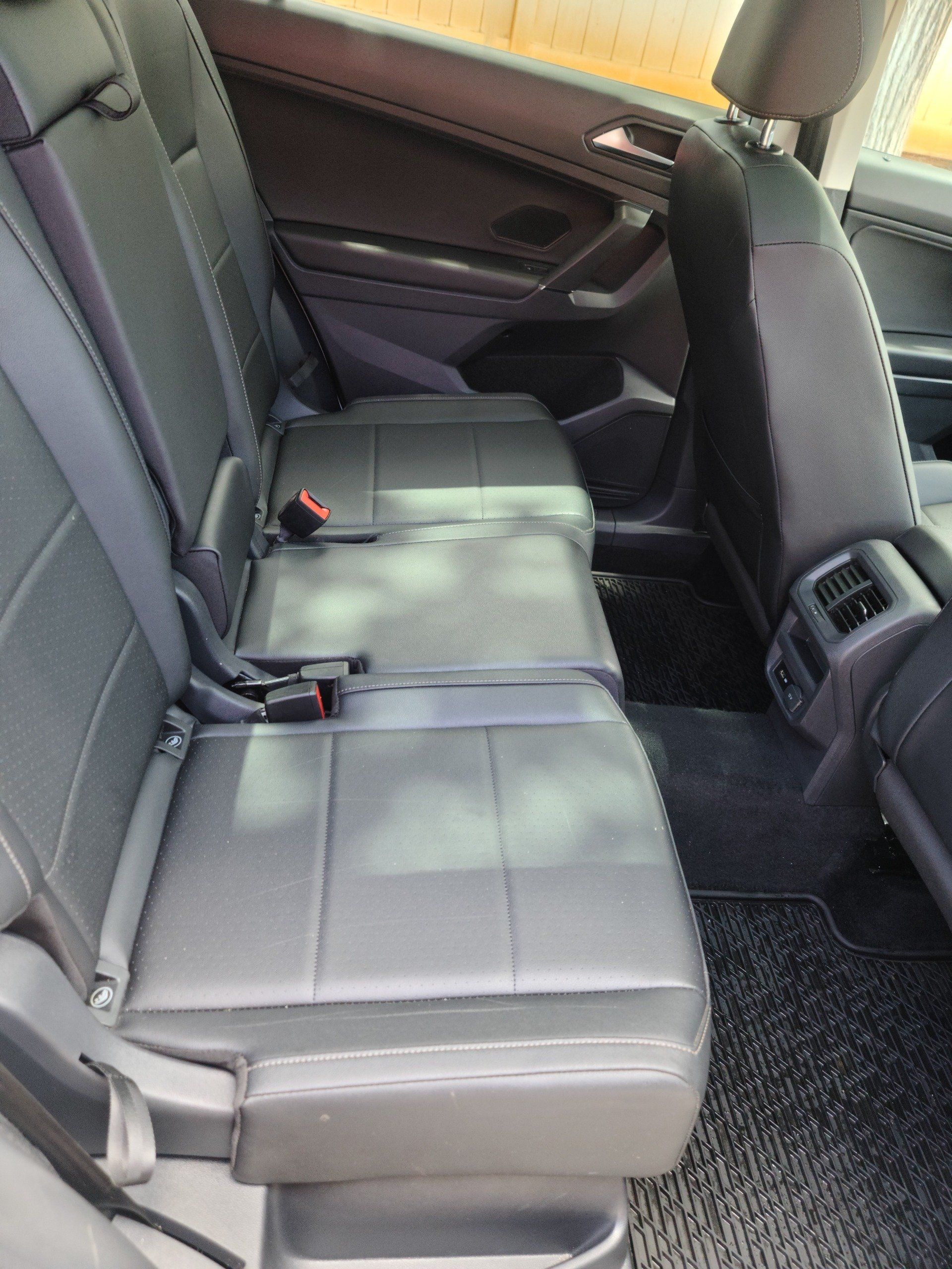 Rear black leather car seats with seatbelts, inside a vehicle.