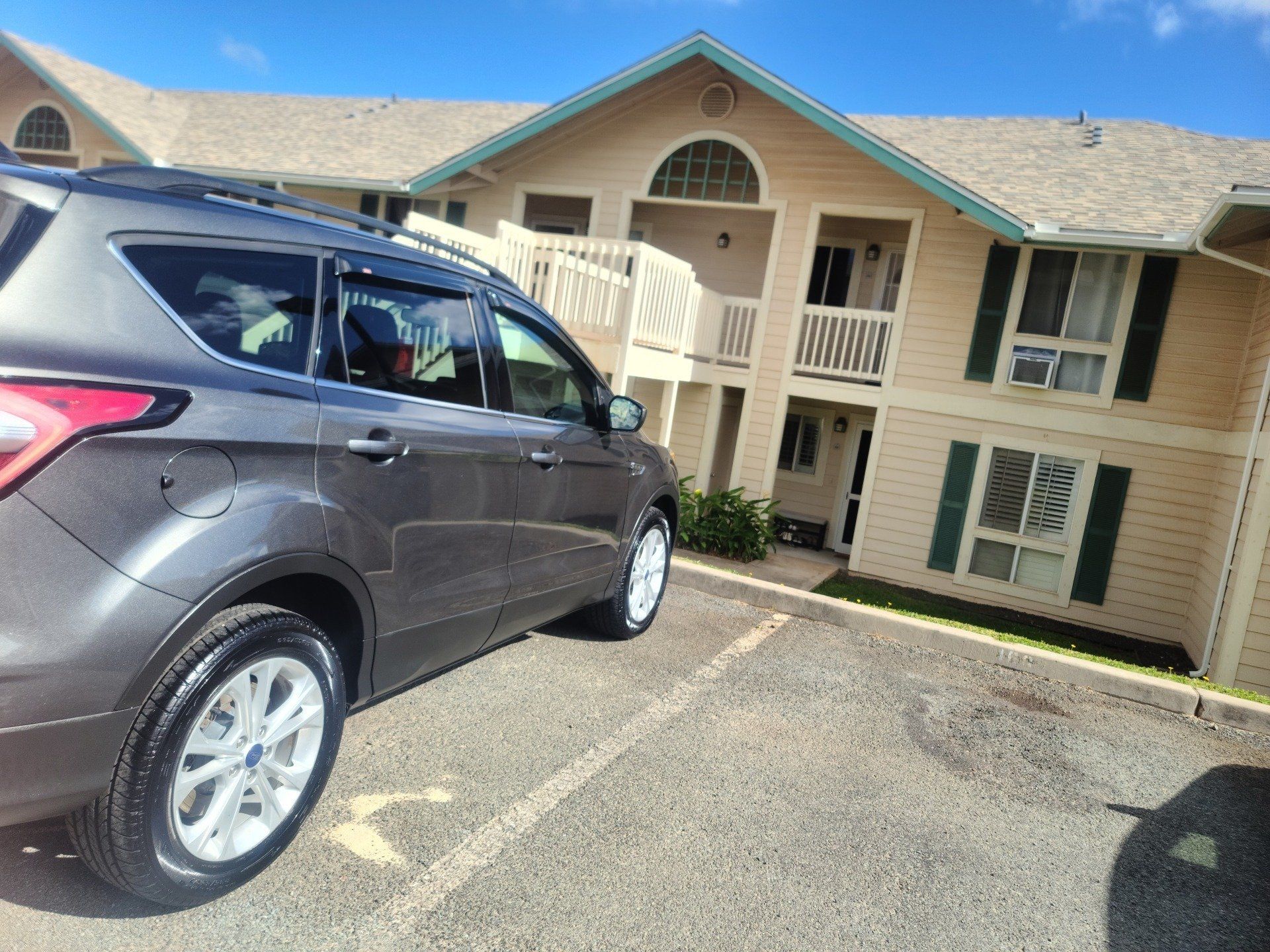 Gray SUV parked in front of a beige apartment building with green shutters and a balcony.