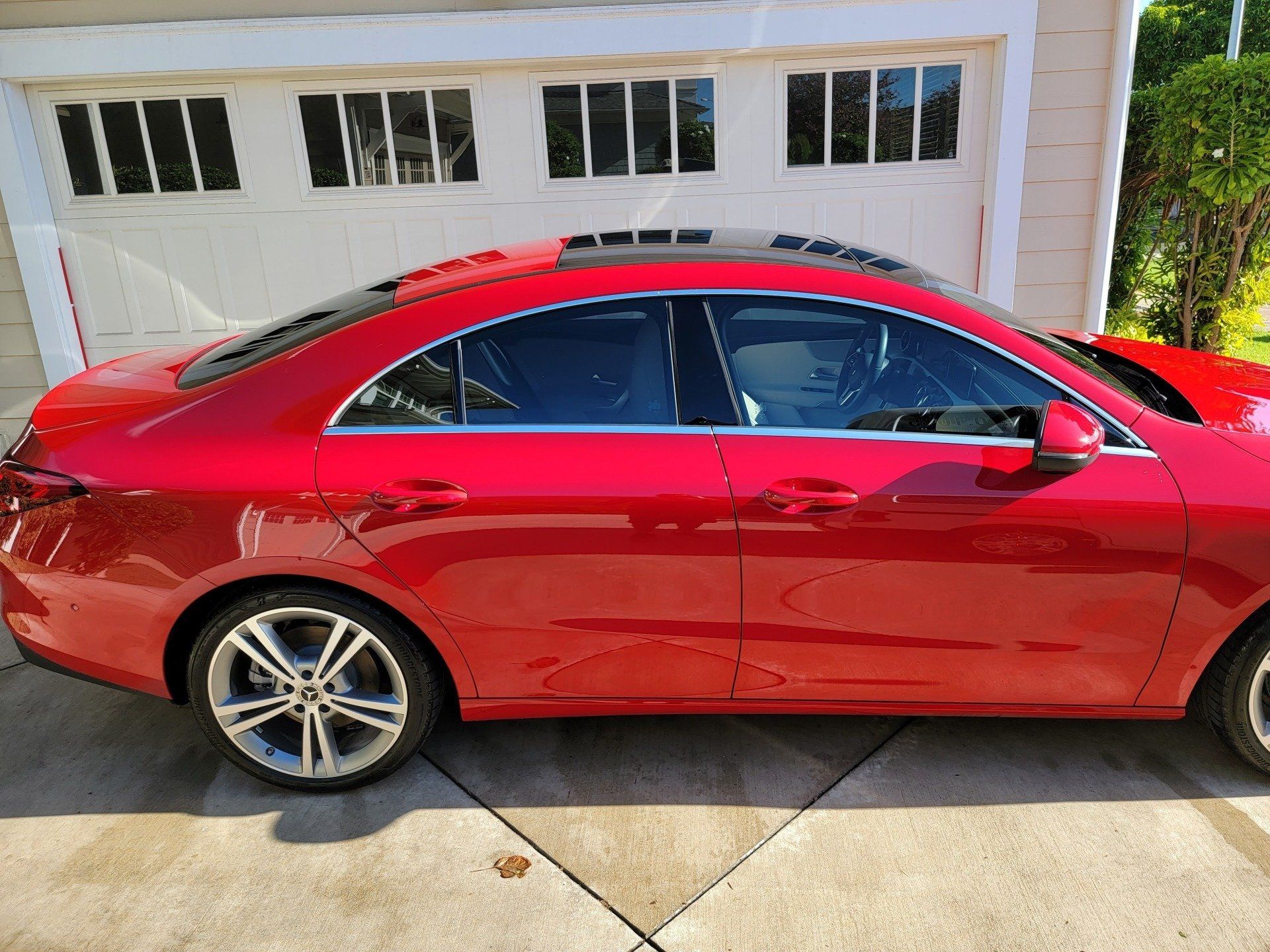 Red Mercedes sedan parked in front of a white garage. The car has tinted windows and a sunroof.