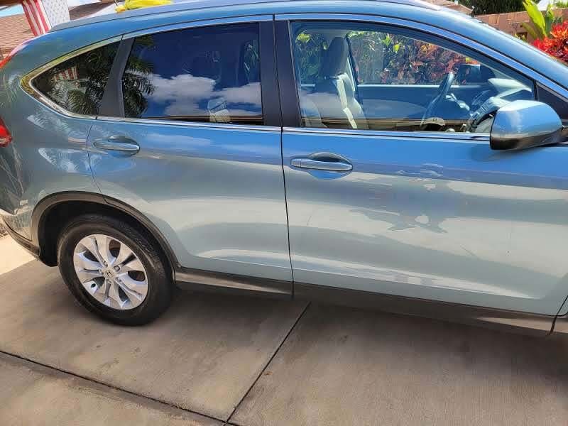 Blue Honda CR-V SUV parked on a concrete driveway, side view. Dark tinted windows, black trim, and silver wheels.