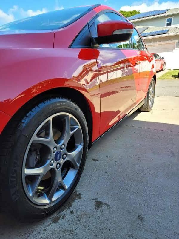 Red Ford Focus, side view, on concrete, sunny day.