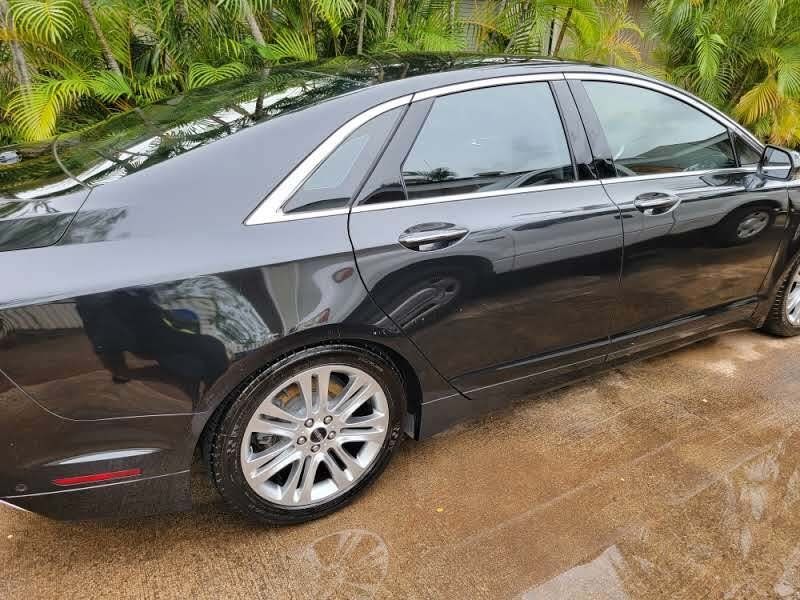 Black sedan with silver wheels, parked on wet pavement near greenery.