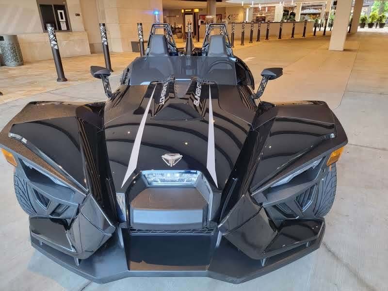 Black Polaris Slingshot three-wheel vehicle parked in front of a building with an entrance.