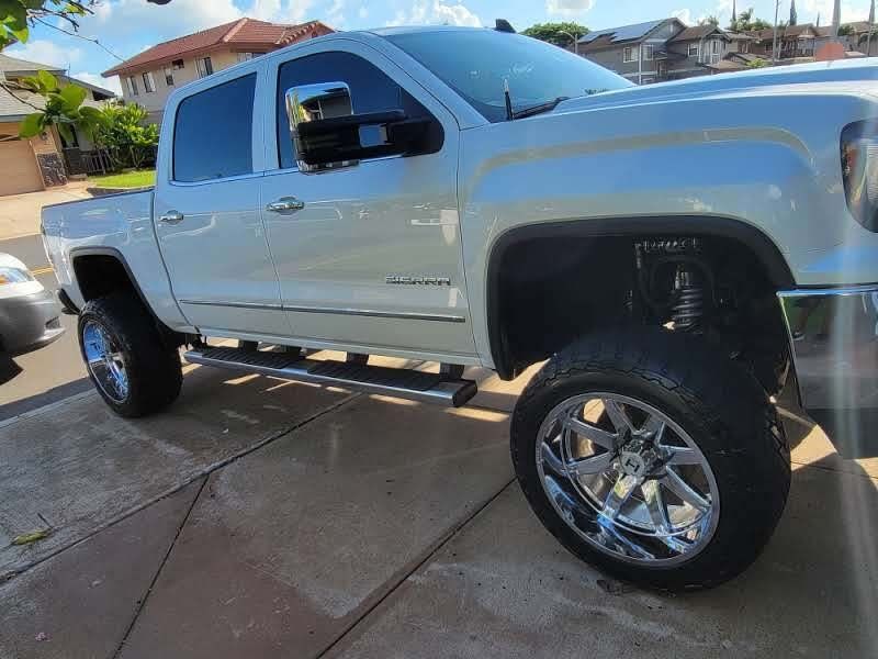White lifted pickup truck with chrome wheels parked on a driveway.