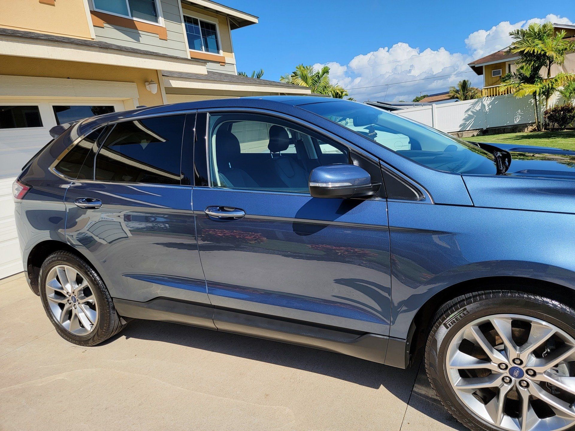 Blue Ford Edge SUV parked in front of a house on a sunny day.