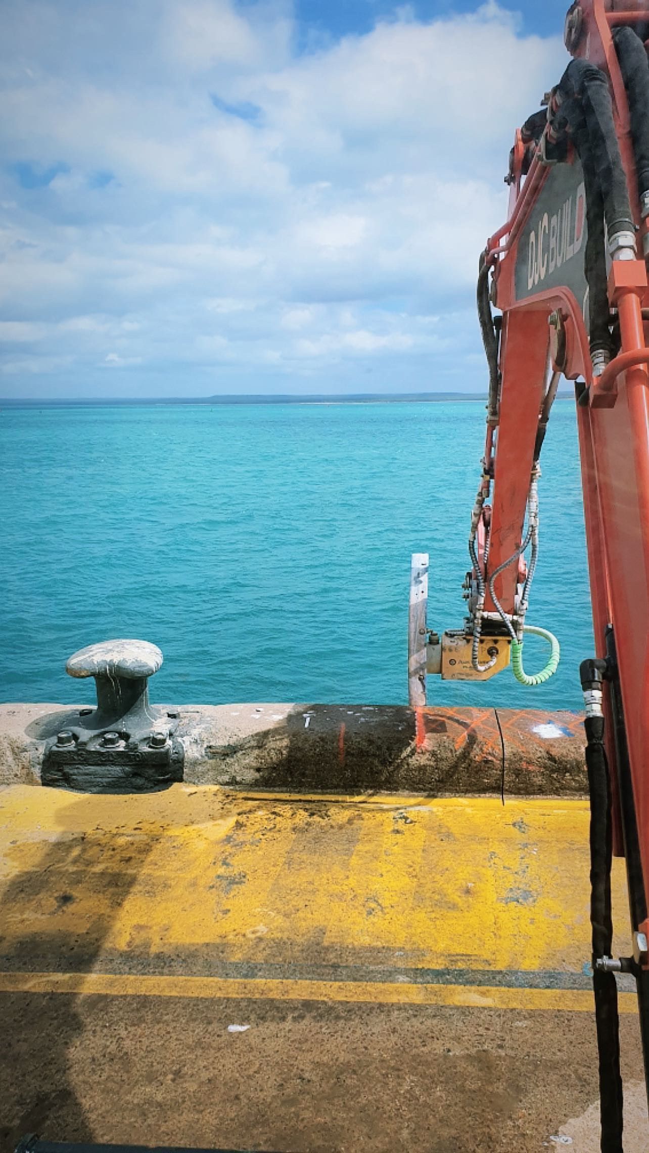 A red crane is sitting on a dock next to a body of water.