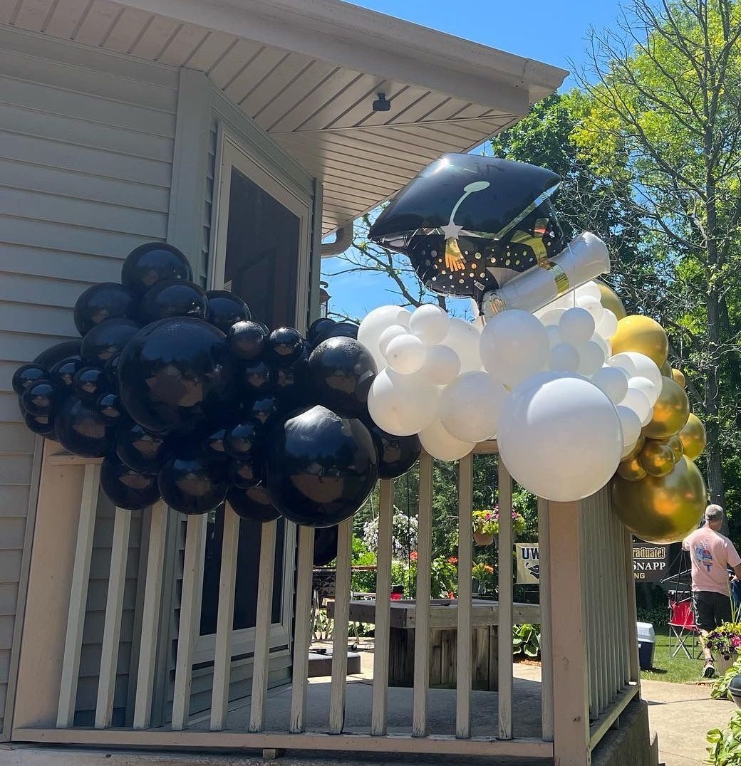 A porch decorated with black and white balloons and a graduation cap