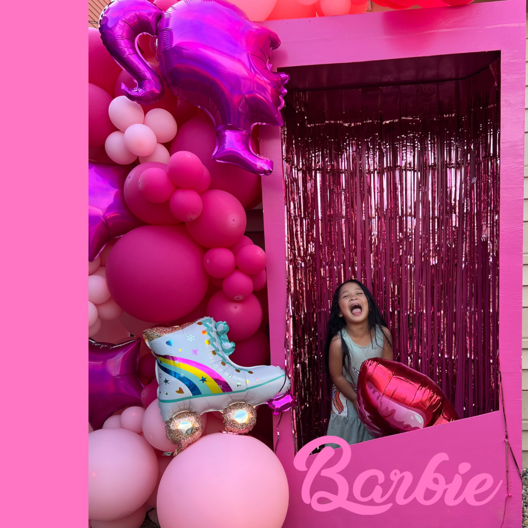 A little girl is standing in a pink barbie photo booth