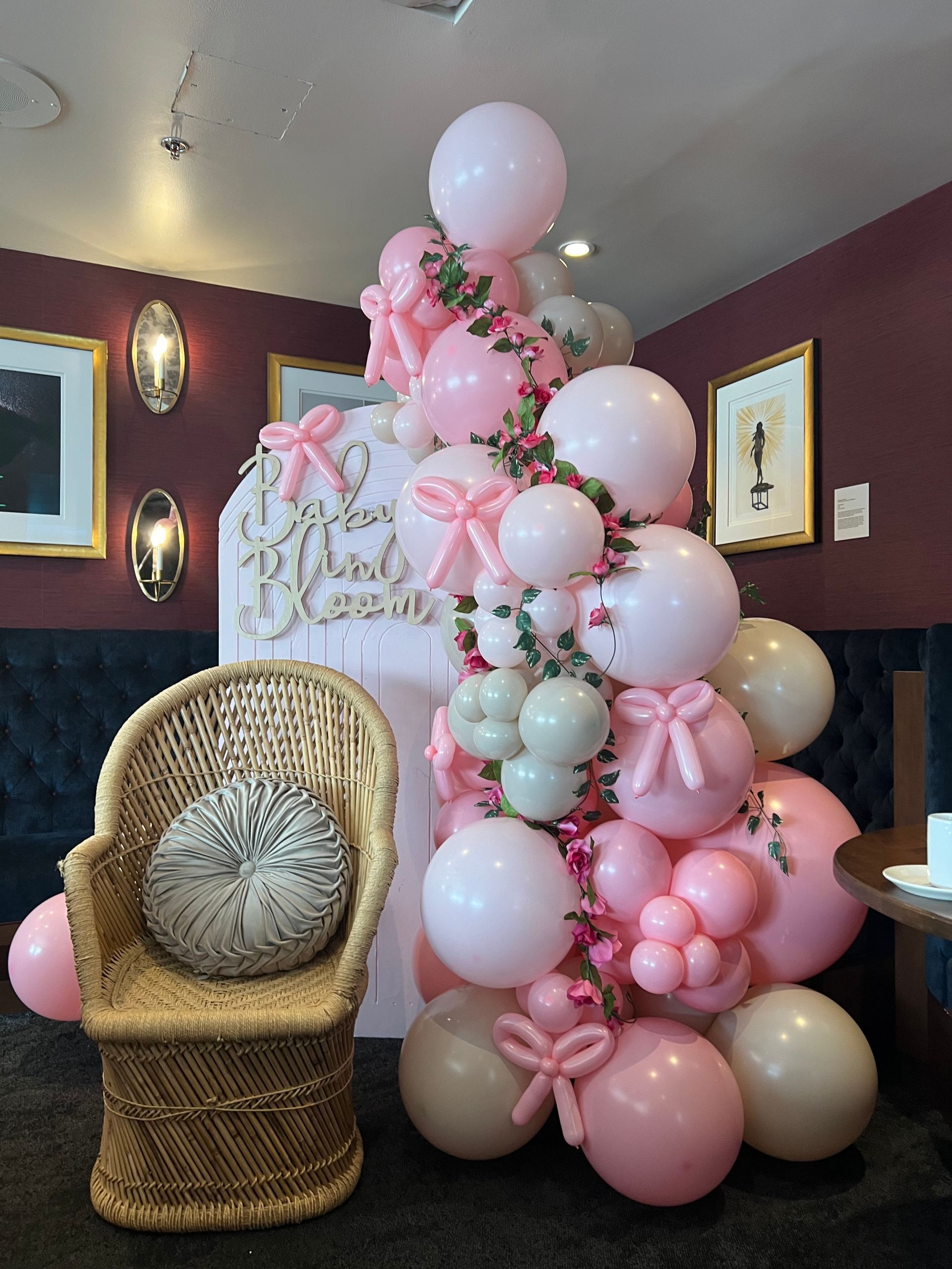 A wicker chair is sitting in front of a wall decorated with pink balloons.