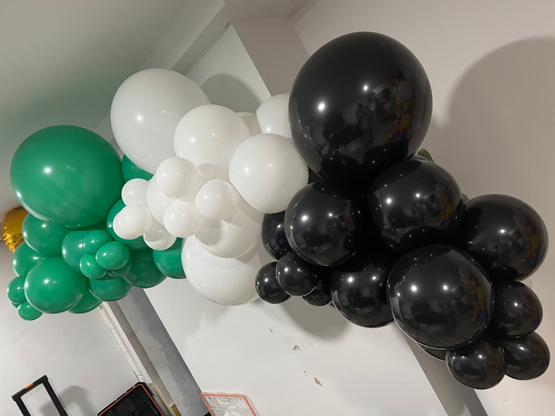 A bunch of black , white and green balloons are hanging from a wall.