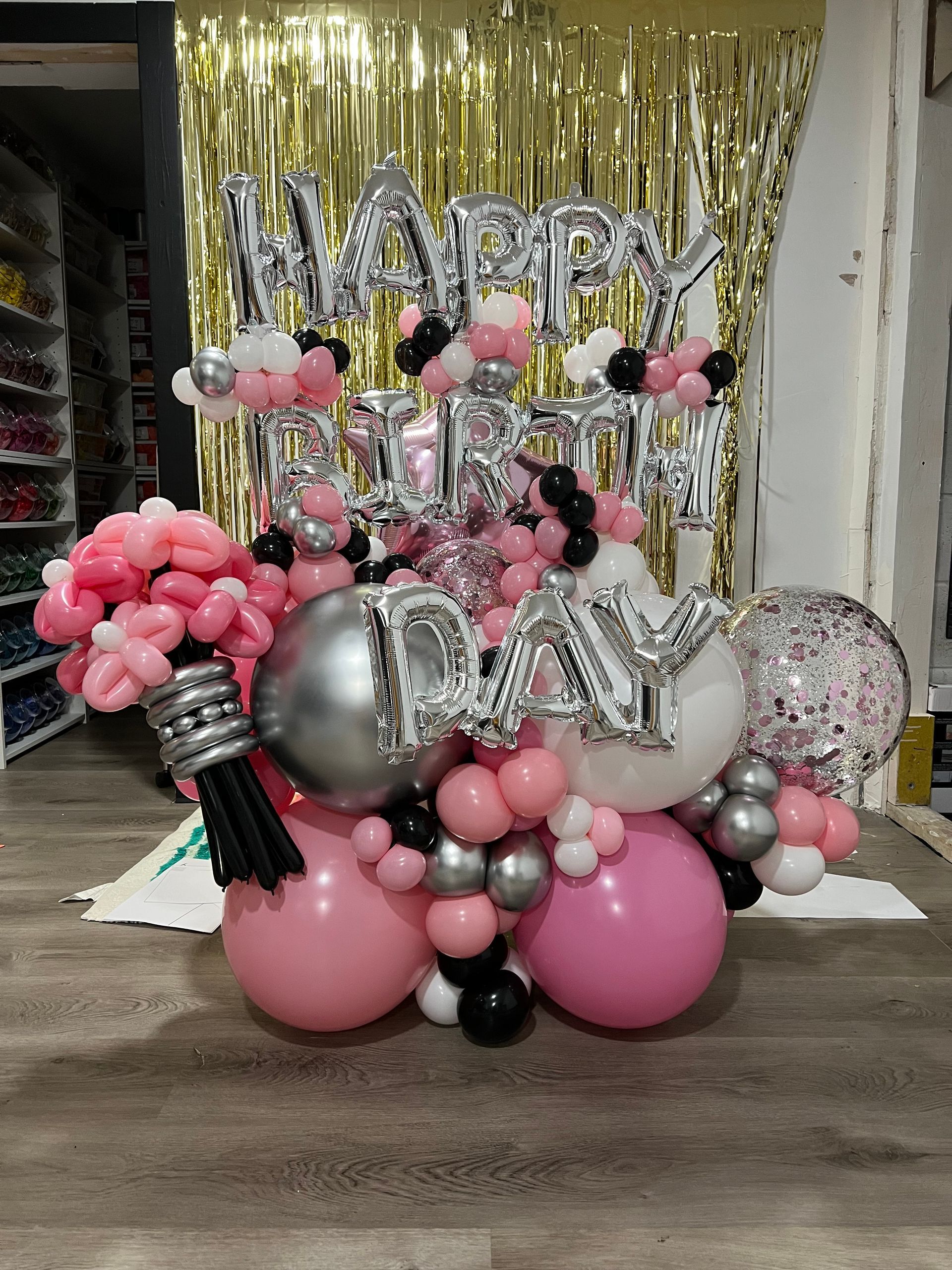 A bunch of pink and silver balloons are sitting on a wooden floor.