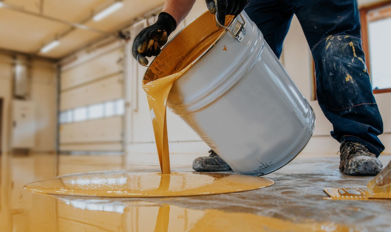 A man is pouring yellow paint into a bucket.