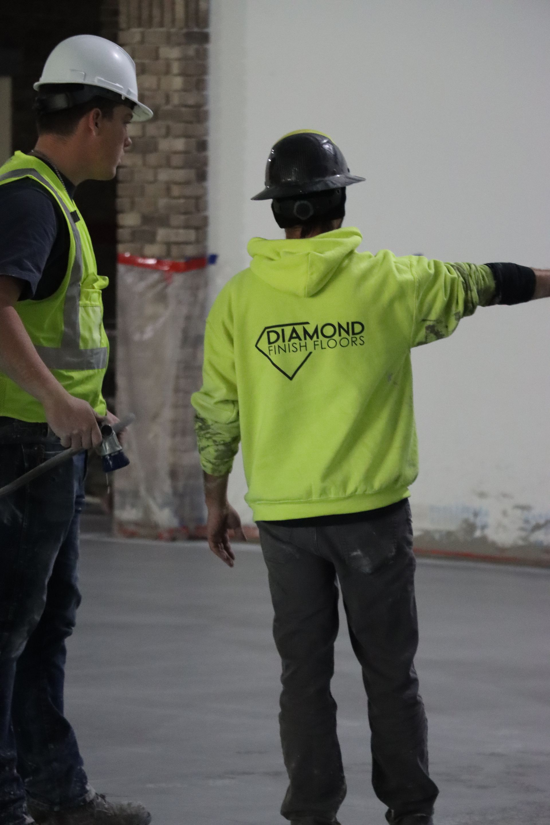 Two construction workers wearing hard hats and safety vests are standing next to each other.