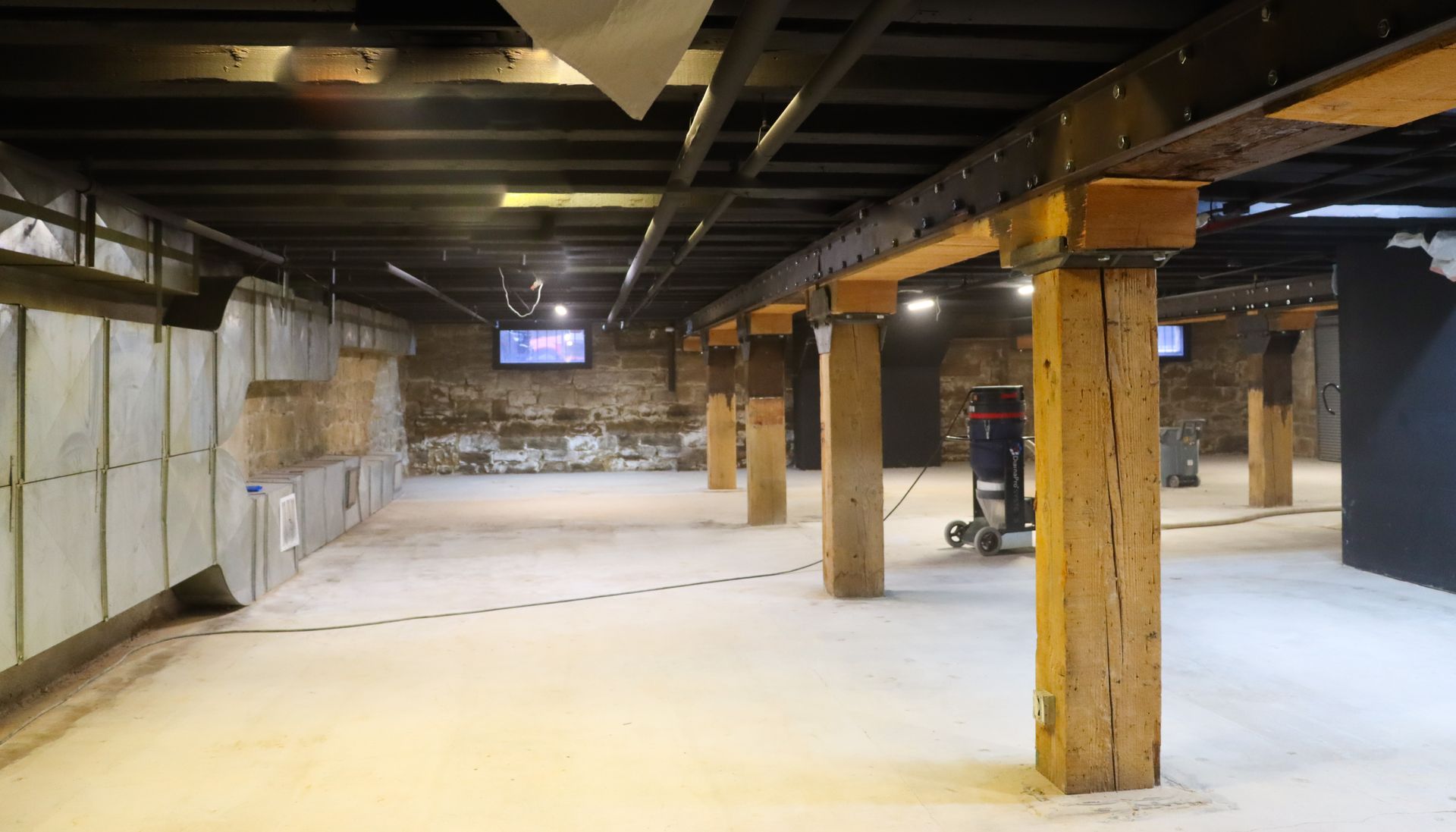 A large empty room with wooden pillars and a television on the wall.