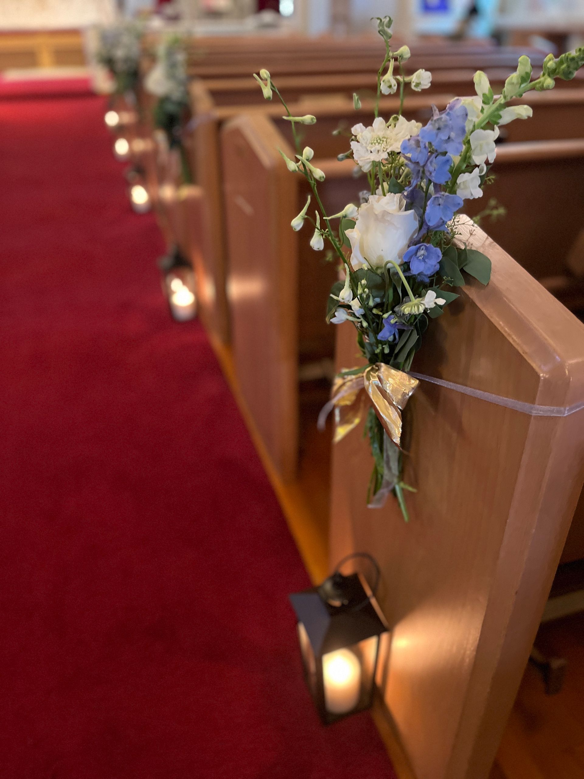 A row of church pews decorated with flowers and candles for a wedding.