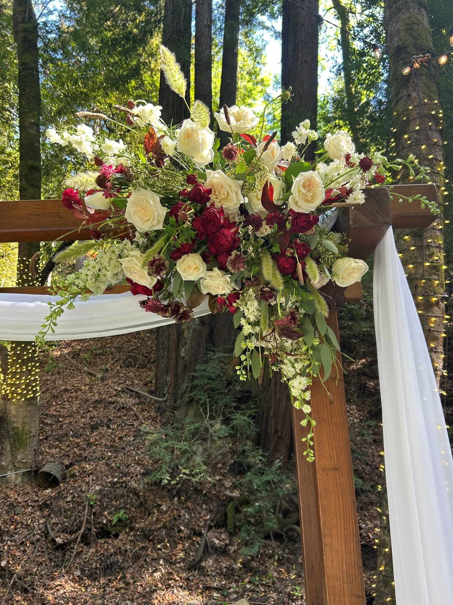 A wooden arch with flowers on it in the woods.