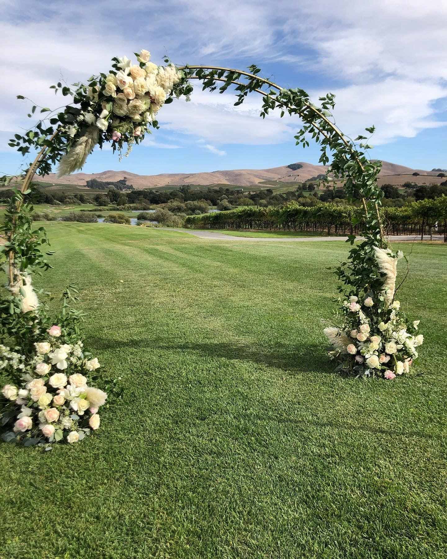 A wedding arch decorated with white flowers and greenery in a wine country golf course