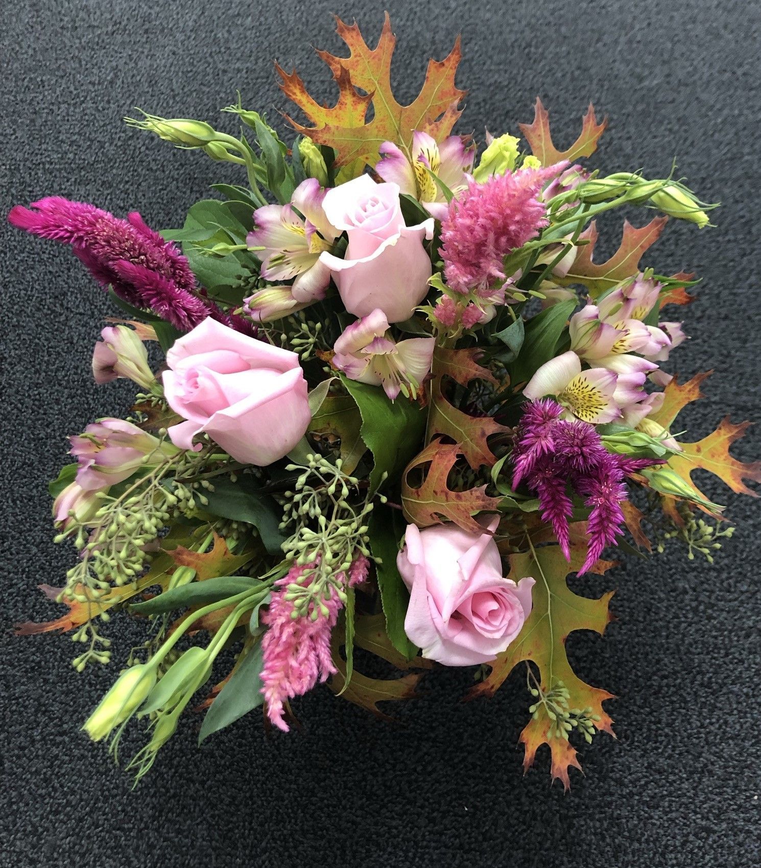 A bouquet of pink roses and purple flowers on a black surface
