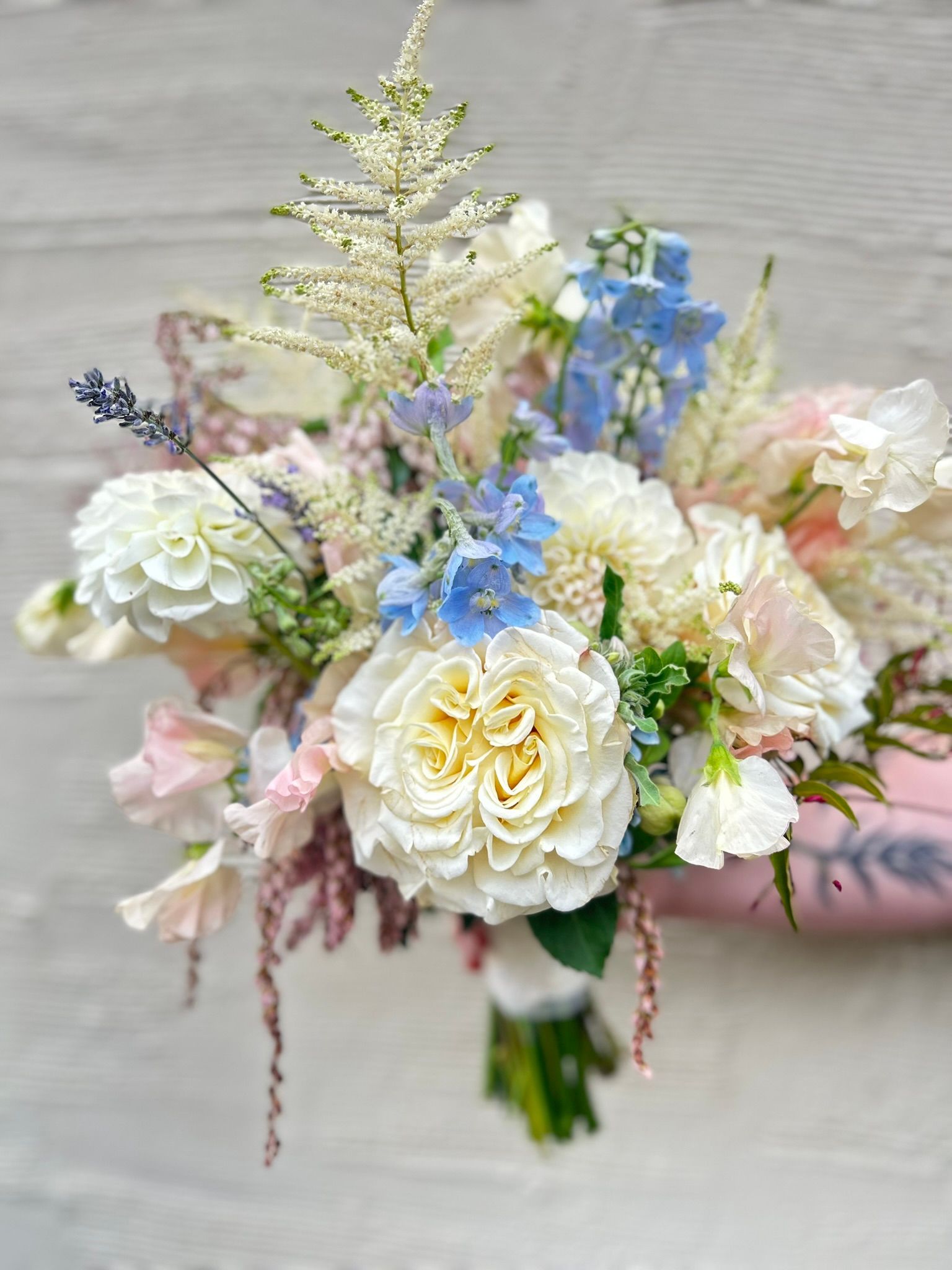 Bouquet of white and blue flowers, including roses and delphiniums, held against a light background.