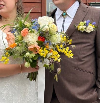 A bride holding a bridal bouquet of wildflowers and groom with a pocket boutonniere