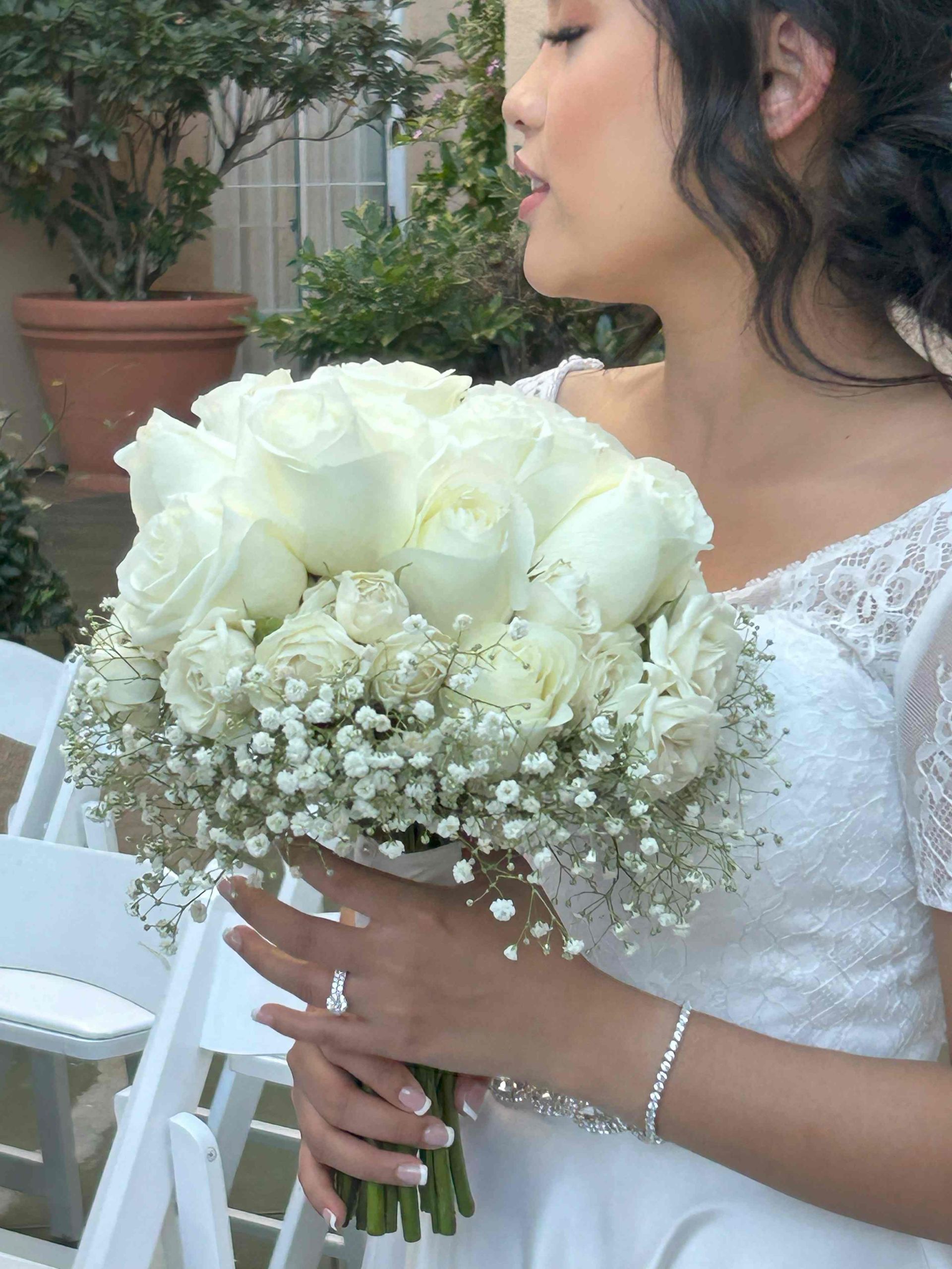 A woman in a white dress is holding a bouquet of white roses and baby 's breath.