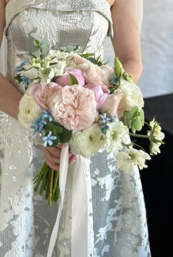Woman in white dress holding a bouquet of pink and white flowers with blue accents and a light pink ribbon.