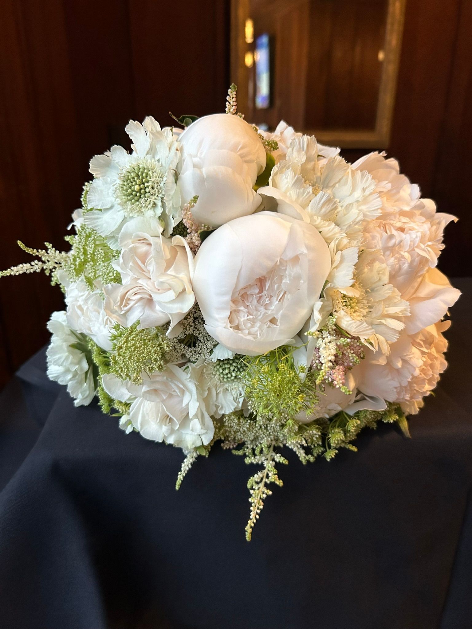White peony and carnation bouquet on a black surface, with some green foliage.