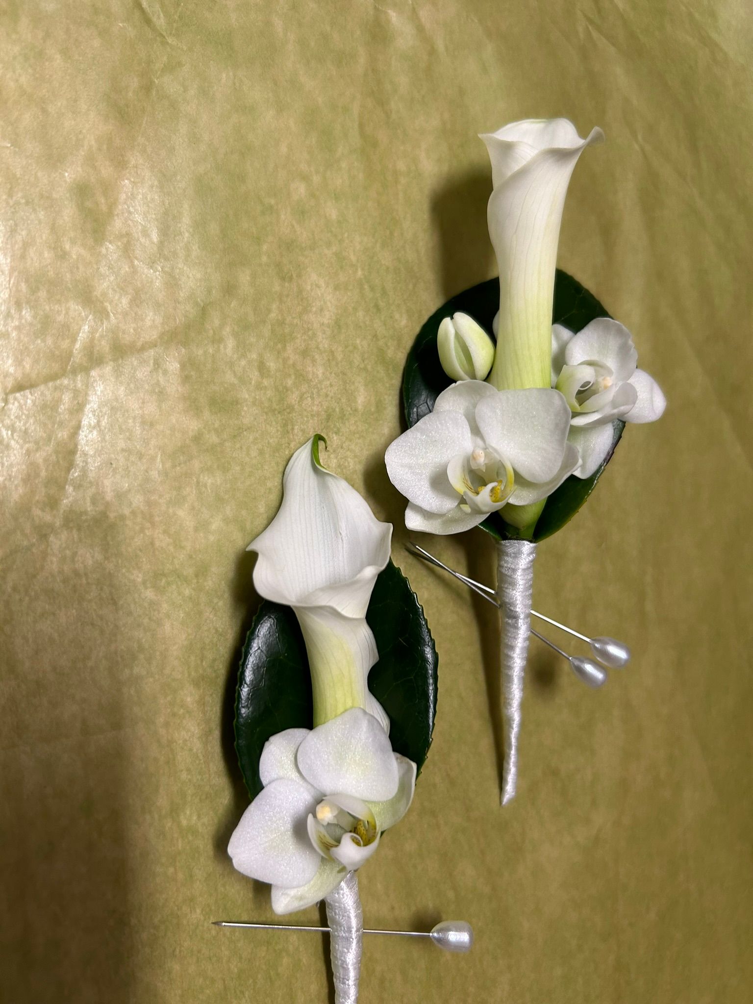 Two white flowers are pinned to a green leaf on a table.