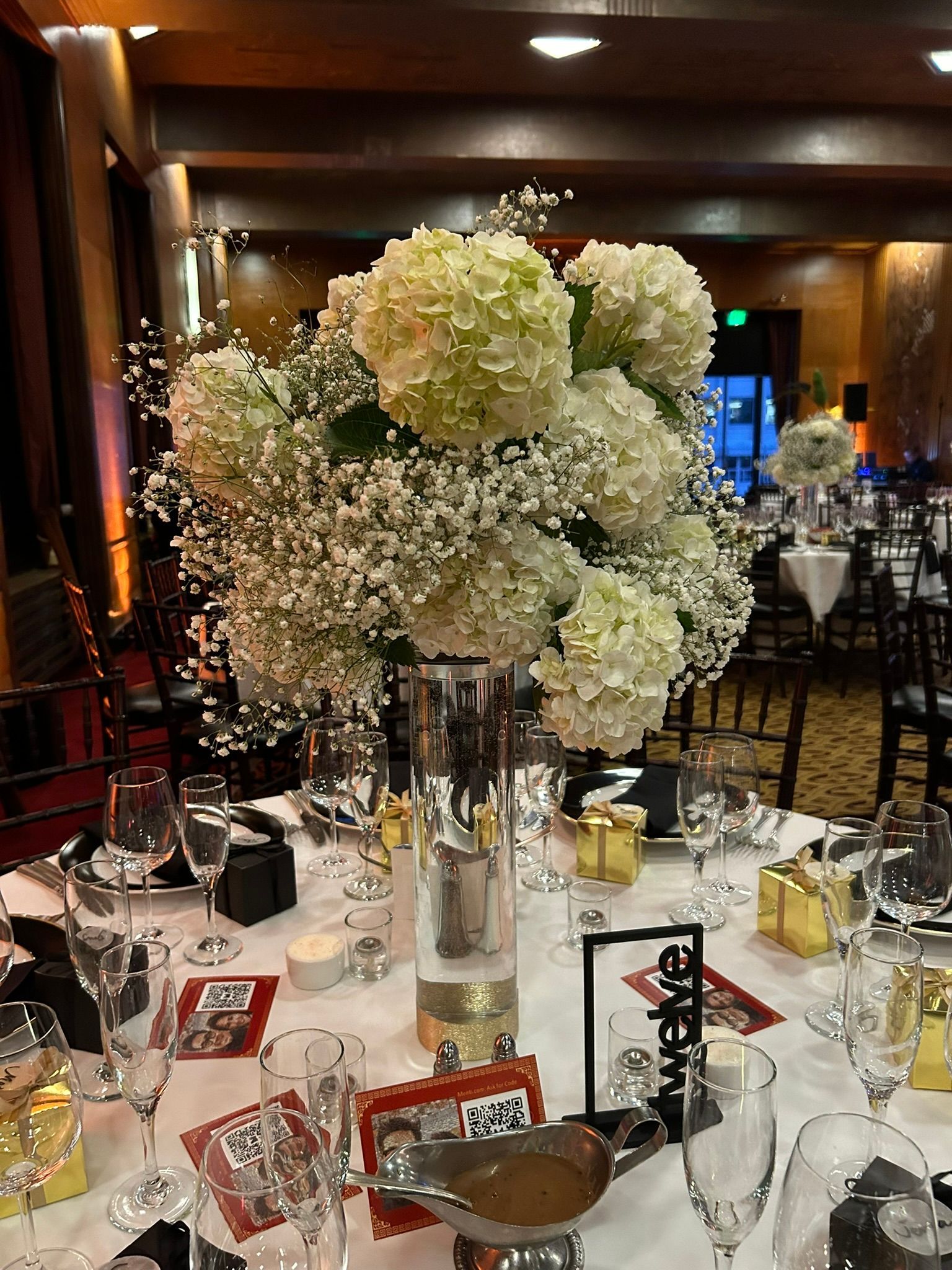 A table set for a wedding reception with a vase filled with white flowers.