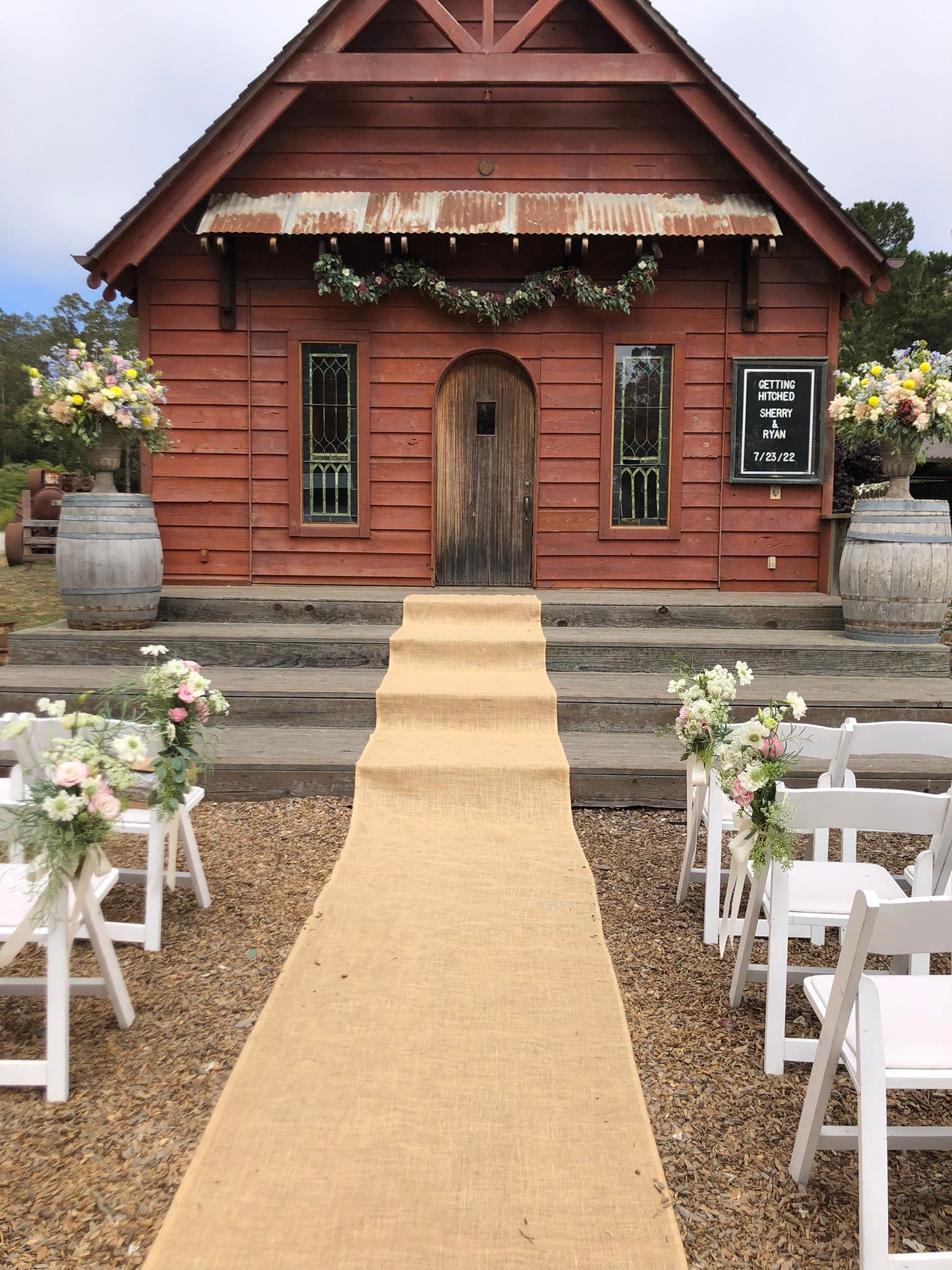 A wedding ceremony is taking place in front of an old church decorated with garland.