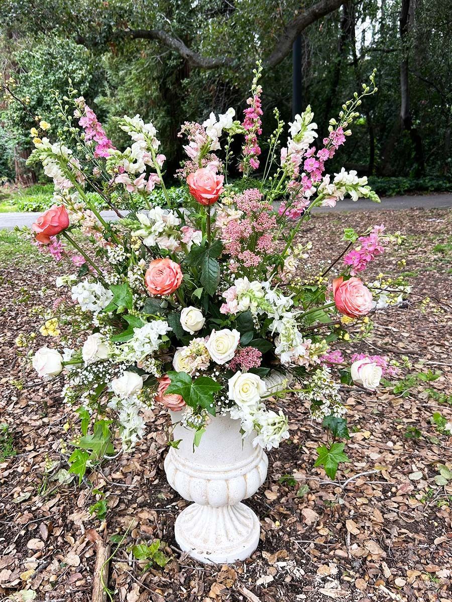 A large urn filled with pink and white flowers is sitting for a wedding ceremony.