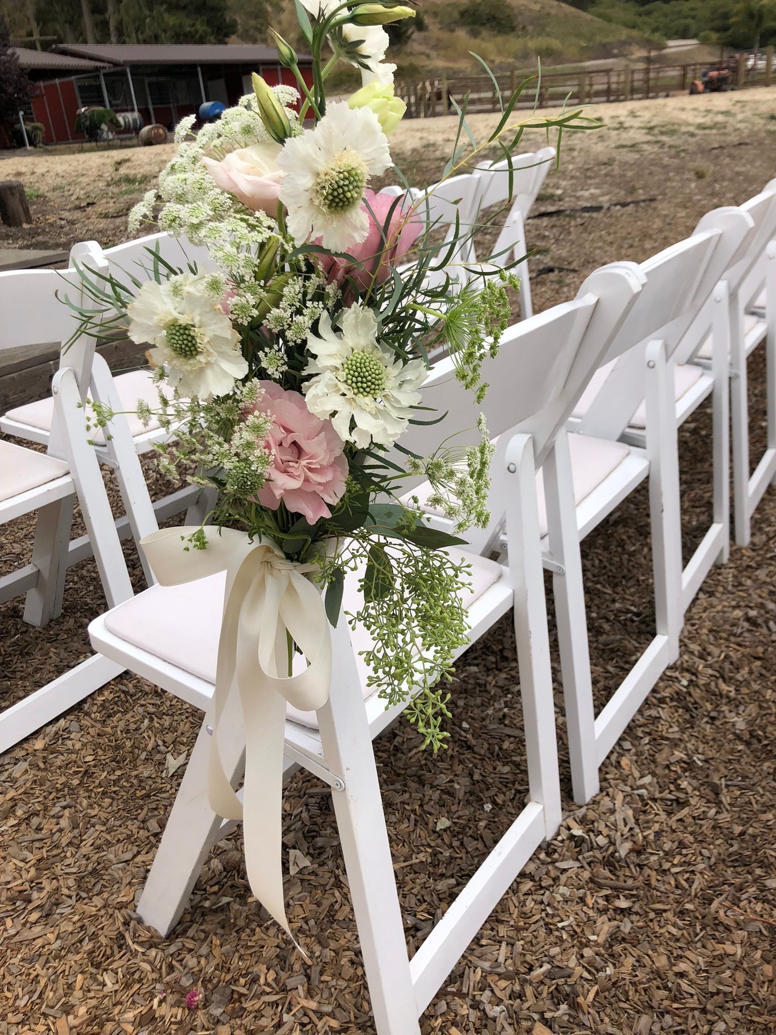 A row of white folding chairs with flowers on them.