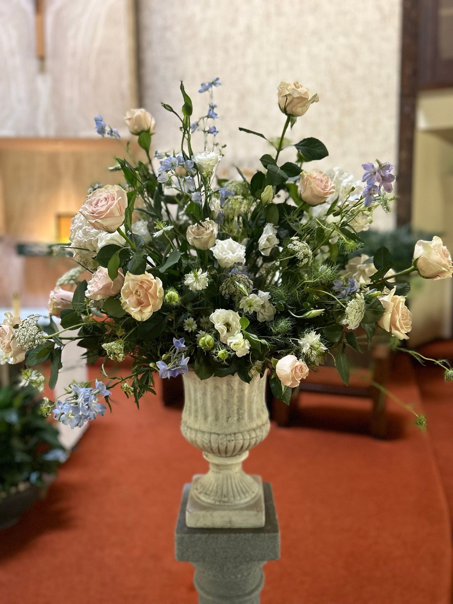 A vase filled with flowers is sitting on a pedestal in a church.