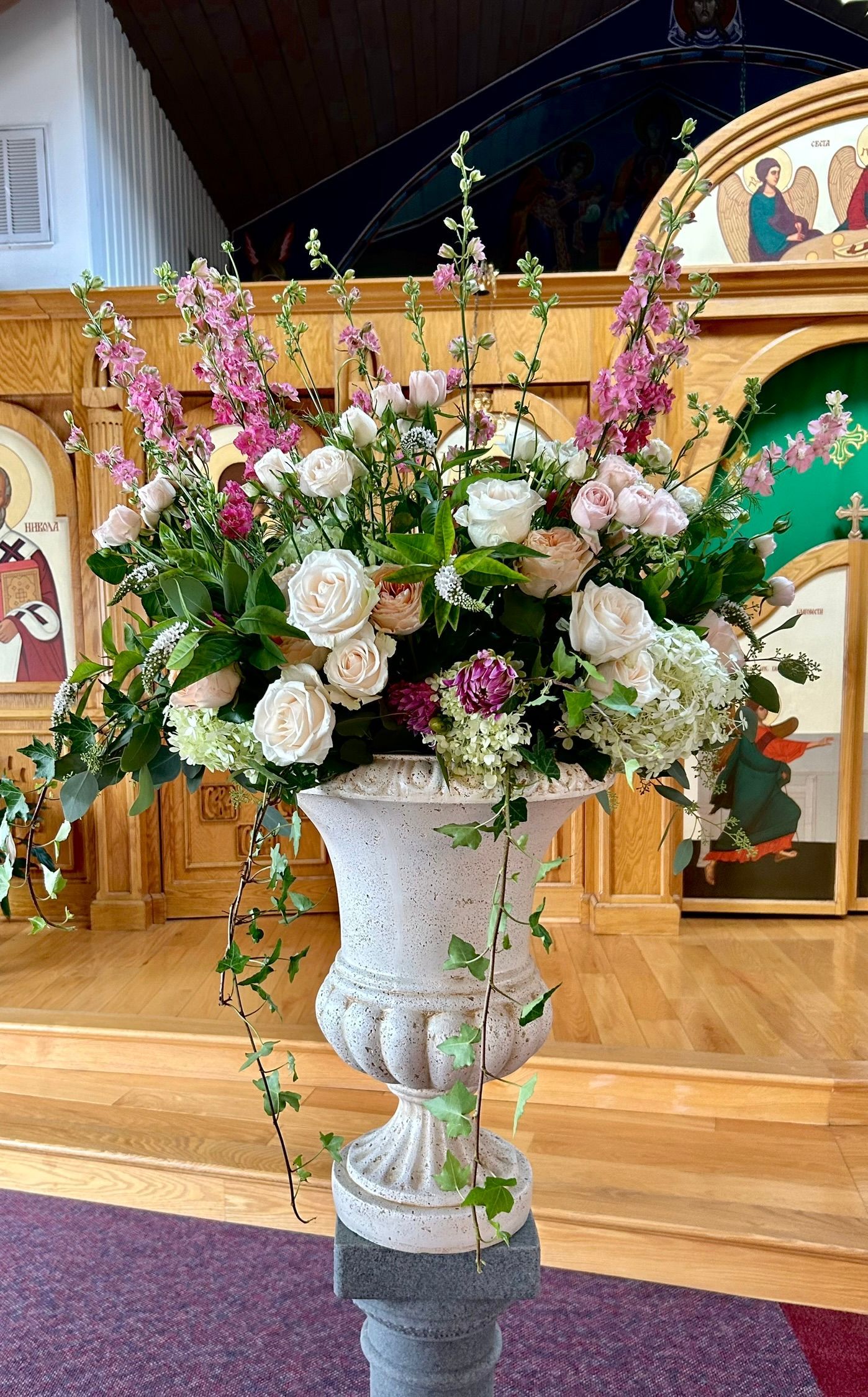 A large urn filled with white and pink flowers is sitting on a pedestal in a church.