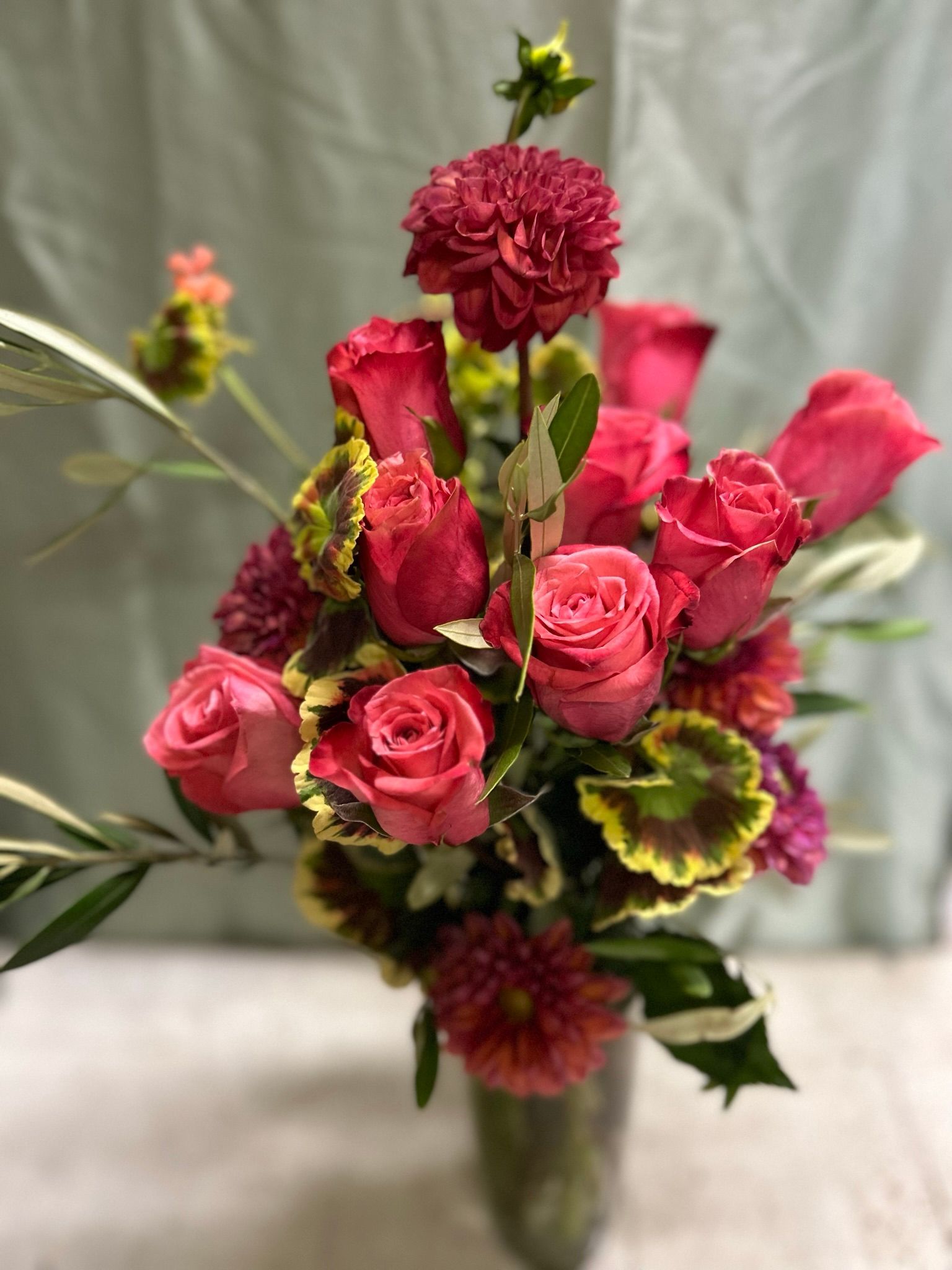A vase filled with pink roses and other flowers is sitting on a table.